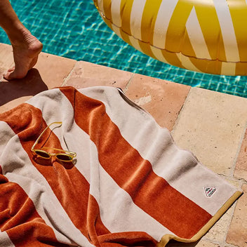 Striped terracotta and ecru beach towel laid by the edge of a swimming pool.